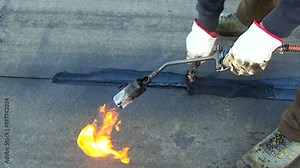 Worker performs sealing overlapping bitumen sheets on the flat roof of the building