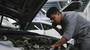 African american male car mechanic looking at an open car engine and talking on a smartphone Free Stock Video Footage
