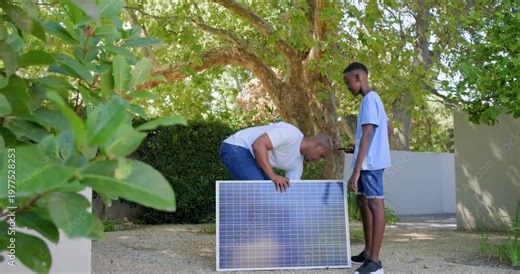 African American father and son arriving in yard, placing solar panel, checking phone for sunlight