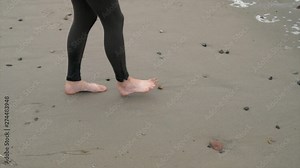 This slow motion close up video shows anonymous bare feet walking along wet beach sand.
