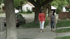Two women walking on neighborhood sidewalk.