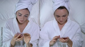 Two girls scrolling gadgets in bed top view, absorbed in internet, generation z