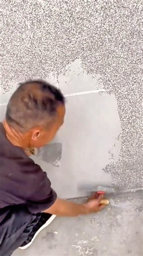worker uses a hand scraper to apply a textured grey coating to a wall