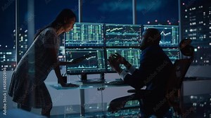 Financial Analyst Talking to Investment Banker in the Evening at Work. Chatting About Real-Time Stock Chart Data on Multi-Monitor Workstation. Businesspeople Have a Meeting in Broker Agency Office.