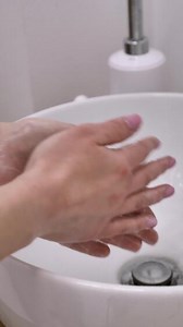 A female nurse beautician washes her hands with disinfectant soap in the washbasin. vertical, close-up