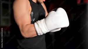 Muscular man in black clothes puts on leather white boxing gloves on his hands before a competition. High quality FullHD footage