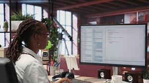 System administrator types code into PC, developing software, entering commands. IT professional at home fixing errors in application, implementing new features, listening music, camera B