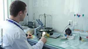 Young male doctor viewing through microscope, taking off his protective mask and smiling