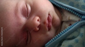 Close-up Newborn Baby Face Portrait Early Days in Macro Sleeping And Smiling Through Dream in blue warm jacket. Child sleep At Start Minutes Of Life. Infants, Childbirth, First Moments Of Borning