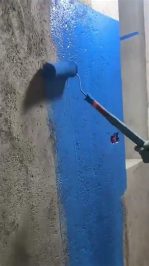 applying blue paint to the rough concrete wall surface using a paint roller evenly