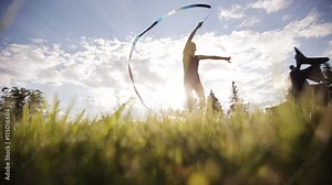 Rhythmic gymnastics. Dance young gymnast with ribbon on sunset sky background.
