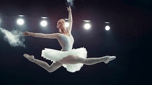 Portrait of a Talented Ballet Dancer Performing on Stage. Young Female Making a Split Leap Jump and Releasing Powder From Her Hands in a Dark Studio. Cinematic Super Slow Motion Speed Ramp Footage