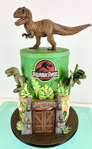 1.4M views · 28K reactions | A recent two-tier tribute to the iconic Jurassic Park original, made of chocolate and vanilla cake, with all details made from fondant. And including a handcrafted sugarpaste Velociraptor, Dilophosaurus and topped with the king of the dinosaurs… the T-Rex of course 練秊 | Samantha Winter | Facebook