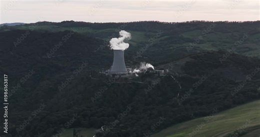 Larderello, Italy - 15 April 2026: Aerial view of Enel Green Power geothermal power plant with steam rising from the cooling tower amidst the rolling hills of Tuscany.