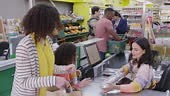 Friendly cashier helping mother and daughter customers bag food...