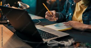 Close-up of girl's hands taking notes with pencil in notebook, laptop, headphones, teenage girl has remote lessons, distance learning, online school.