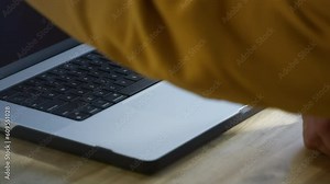 An old man opens a laptop in a restaurant. Remote work of a freelancer in a coworking. Grandpa is an IT technician or programmer. Fashionable Senior male hipster in a cafe. Modern and stylish look.