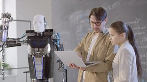 Medium footage of young modern teacher explaining female mixed race student how to make humanoid robot follow commands using laptop as remote control