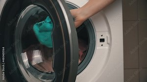 Women's hands put clothes in a modern washing machine. The girl carefully cleans clothes with detergent, washing powder, rinse aid in the laundry room. Cleanliness, hygiene, bathroom.