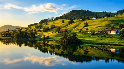 Sunlit green hills and farmhouses by a tranquil lake