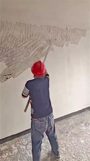 removing old white plaster from indoor wall with a long manual scraper during home renovation work