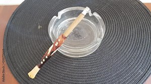 Smoldering cigarillo with a wooden mouthpiece in an ashtray with ash