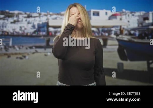 Woman covering nose and mouth with hands in studio against a beach harbor backdrop; discomfort illness Stock Video Footage - Alamy