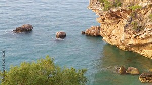 Beautiful morning seascape. Aerial top view of charming calm blue sea water, huge rocks and stones, green trees. Scenic summer marine background. Real time full hd video footage.