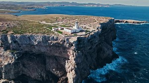 Drone view of a lighthouse scenic viewpoint offering dramatic sea views. Aerial view of the most northerly point of the lighthouse at Cap de Cavalleria, Menorca.