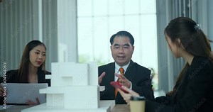 Group of business professionals gathers around a table, engaging in lively discussion while examining a detailed building model.
