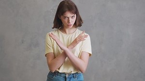 The angry girl in a yellow t-shirt shaking her head negatively and showing no gesture with crossed arms while standing in the grey studio