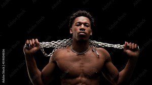 Muscular man showing muscles and holding a chain. African American male posing against black background.