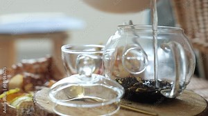 Large leaf black tea is brewed in a transparent teapot. Boiling water is poured and the tea is covered with steam. Boiling water, hot tea. Drops on a glass teapot.