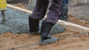 Workers in black rubber boots shovels leveled cement flowing from the concrete pump into the ground for screed floor heating