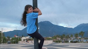 Child climbing a pole in the street. A view of little girl want to climb the pole in the park in the day light.