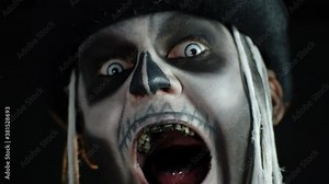 Man with skeleton makeup trying to scare, opening his mouth and showing dirty black teeth and tongue