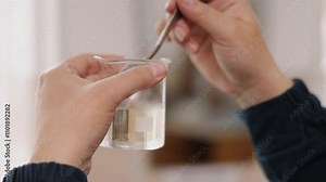 Glass beaker, stirring close-up, small experiment. Close-up view captures hands actively mixing solution in petite glass beaker as part of lab experiment.