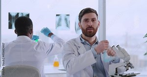 Attractive young doctor scientist in microbiology center smiling to camera using microscope developing and testing samples at vaccination laboratory.
