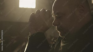 Monk opening eyes and looking up during prayer slow motion close up. Mid adult caucasian man praying with clasped hands in Christian church. Faith and hope concept