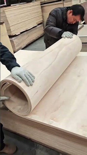 Stacking and rolling large flexible plywood sheets in a woodworking factory workshop.