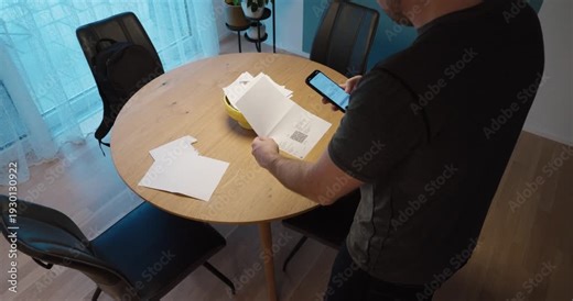 Man scanning a QR code on a paper invoice using a smartphone at a dining table, illustrating digital payment, online banking and modern financial transactions.