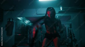 Professional female boxer does cardio or endurance workout before championship fight. Woman exercises with battle ropes in dark boxing gym with LED lighting. Physical activity and CrossFit training.