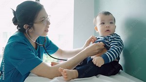 Asian female doctor examining little cute boy with stethoscope in medical room at hospital.