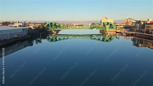 Ascending drone view of the Park Street Bridge captures the quiet drawbridge span, calm channels, and the gradual transition from night to day between Oakland and Alameda.