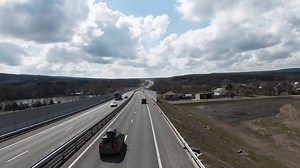 Highway outside the city, panoramic view from above with driving cars. Shot. Straight highway stretching along fields and forests on cloudy sky background.