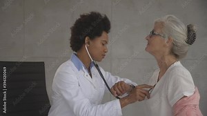 Senior woman with protective facial mask having a medical exam by black female doctor in the office
