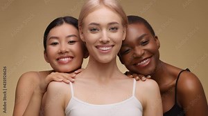 Female friendship and connection. Three happy multiethnic ladies posing over beige studio background, cuddling together