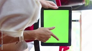 Woman holding mobile tablet computer with green chromakey screen. Scrolling, watching, thumb up gesture. Vertical video footage in café with red chairs