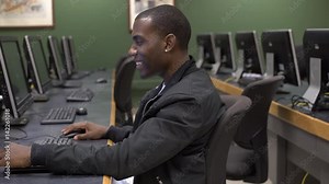 Young male sitting in computer lab smiling at screen.