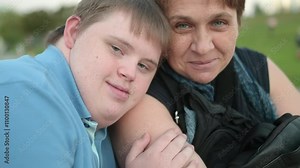 4K video portrait of teenager boy with Down syndrome and his loving mother. Adult son with down syndrome hugs his mom gently